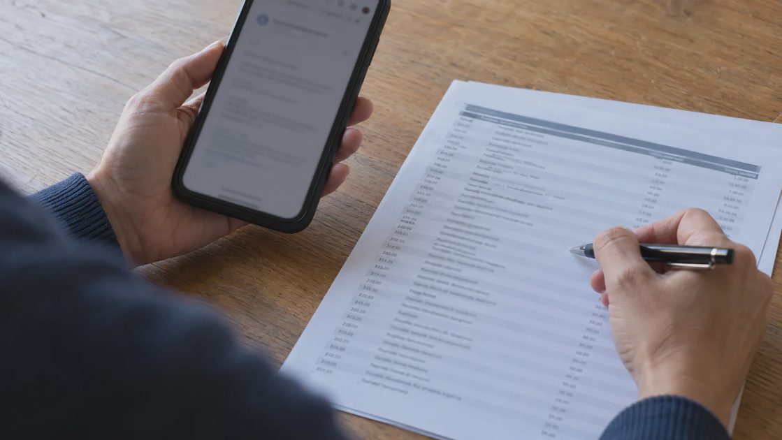 Hands comparing a smartphone message with rows on a printed statement.
